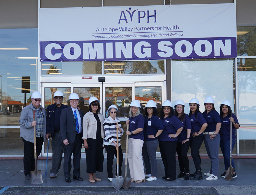 AVPH staff outside the new permanent home behind a Coming Soon banner.